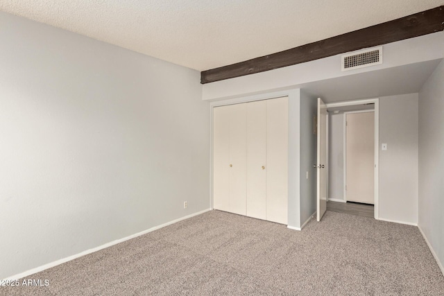 unfurnished bedroom featuring a textured ceiling, a closet, carpet, and beam ceiling