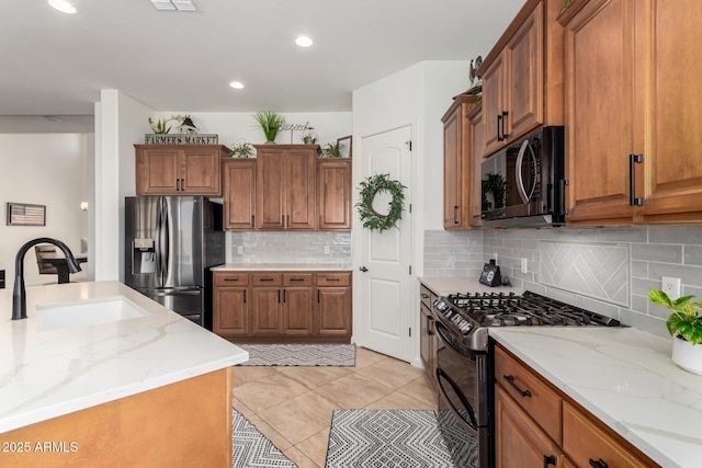 1804 W Magdalena Ln, Phoenix, AZ 85041 - kitchen with black appliances, a sink, brown cabinetry, decorative backsplash, and light stone counters