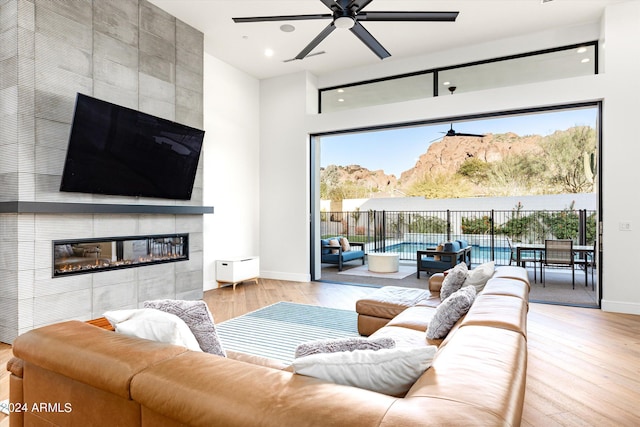 living room featuring a tile fireplace, ceiling fan, and light hardwood / wood-style flooring