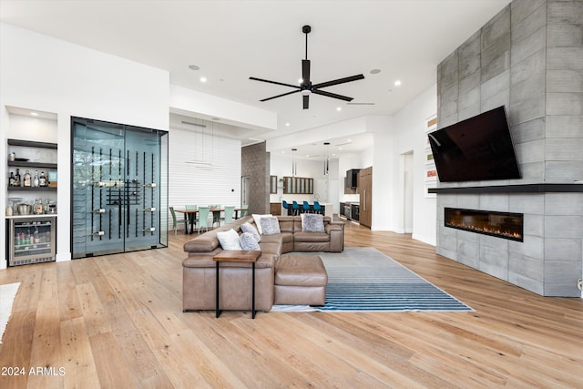 living room featuring ceiling fan, a fireplace, beverage cooler, and light hardwood / wood-style floors