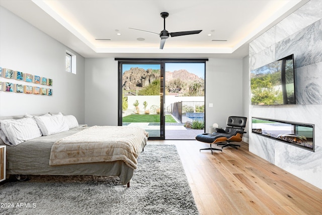 bedroom featuring a fireplace, hardwood / wood-style flooring, access to outside, ceiling fan, and a raised ceiling