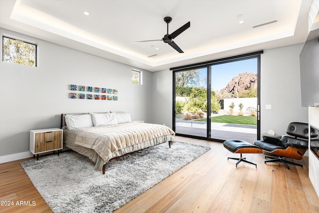 bedroom featuring a raised ceiling, access to outside, and hardwood / wood-style floors