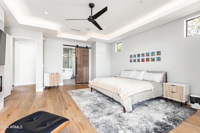 bedroom featuring radiator heating unit, ceiling fan, a raised ceiling, a barn door, and light hardwood / wood-style flooring