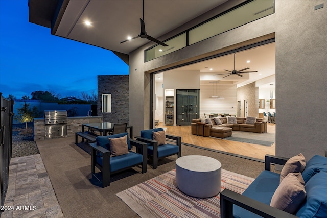 patio terrace at dusk with an outdoor living space, an outdoor kitchen, area for grilling, and ceiling fan