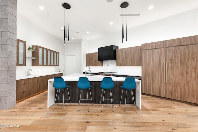 kitchen with a kitchen bar, a center island with sink, light wood-type flooring, pendant lighting, and a high ceiling