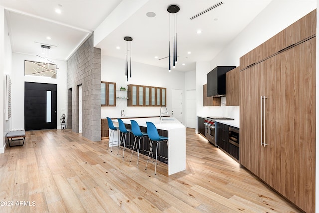 kitchen with a breakfast bar, decorative light fixtures, sink, double oven range, and a kitchen island with sink