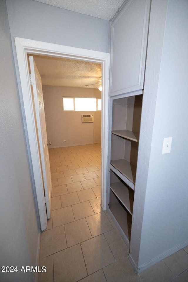 corridor with a textured ceiling, a wall unit AC, and light tile patterned floors