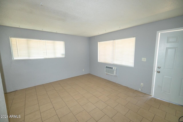 spare room with a textured ceiling, light tile patterned floors, and a wall mounted air conditioner