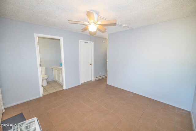 unfurnished bedroom featuring light tile patterned floors, ensuite bathroom, baseboard heating, ceiling fan, and a textured ceiling