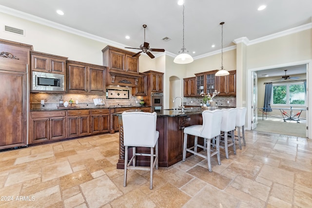 kitchen with a kitchen breakfast bar, dark stone countertops, an island with sink, appliances with stainless steel finishes, and ornamental molding