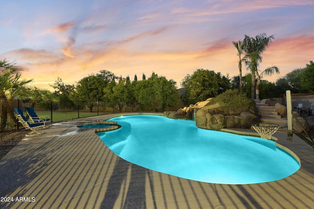 pool at dusk featuring a patio area and an in ground hot tub