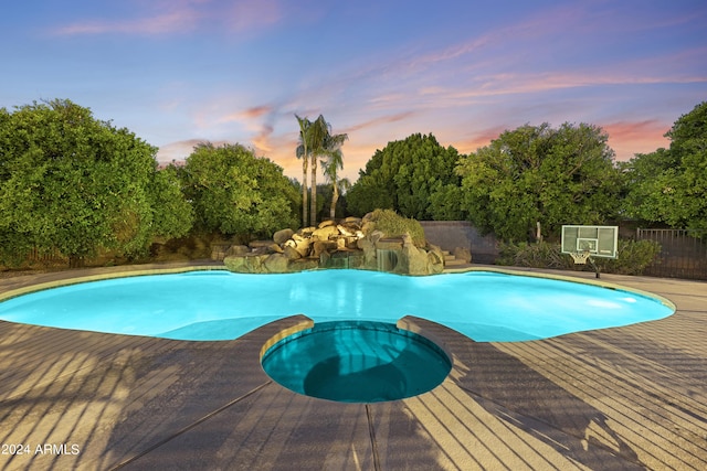 pool at dusk featuring an in ground hot tub