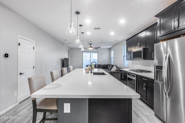 kitchen featuring a kitchen island with sink, a breakfast bar area, stainless steel appliances, ceiling fan, and decorative light fixtures