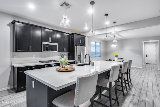 kitchen with appliances with stainless steel finishes, hanging light fixtures, a center island with sink, and a kitchen breakfast bar