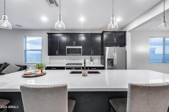 kitchen featuring stainless steel refrigerator with ice dispenser, decorative light fixtures, sink, and an island with sink