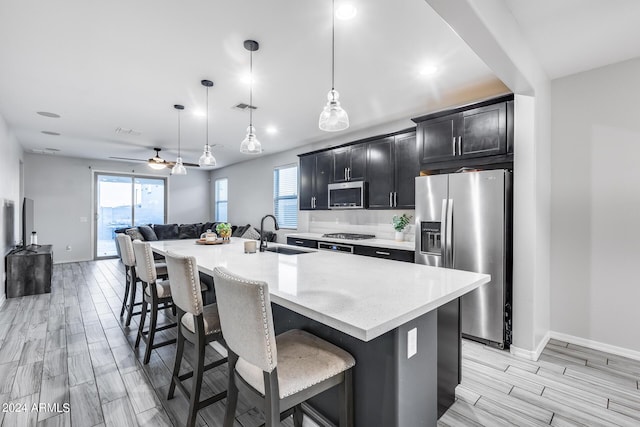 kitchen featuring pendant lighting, stainless steel appliances, a center island with sink, ceiling fan, and sink