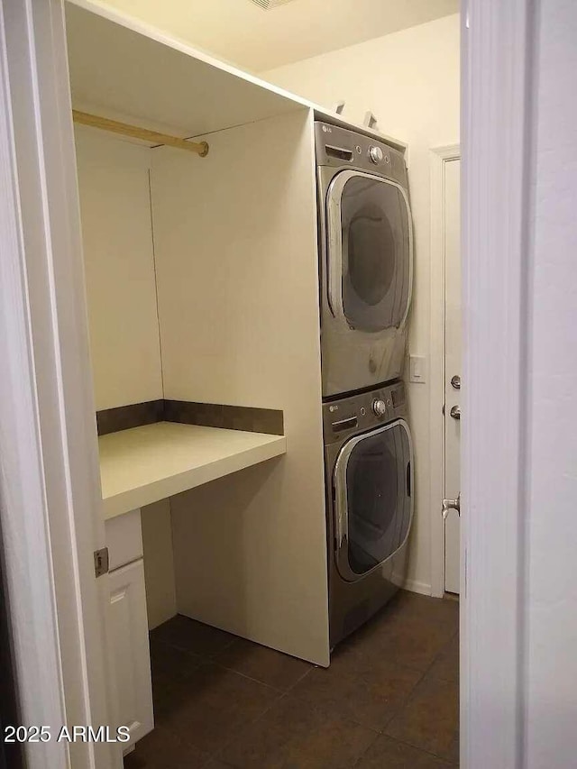 laundry room with dark tile patterned floors and stacked washer / dryer