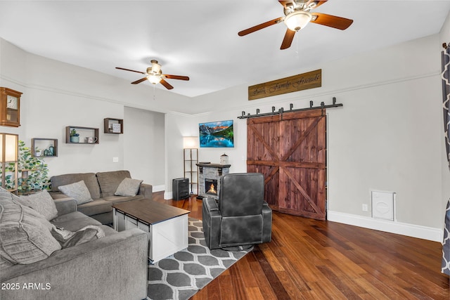 living room with a ceiling fan, a barn door, dark wood-style floors, and baseboards