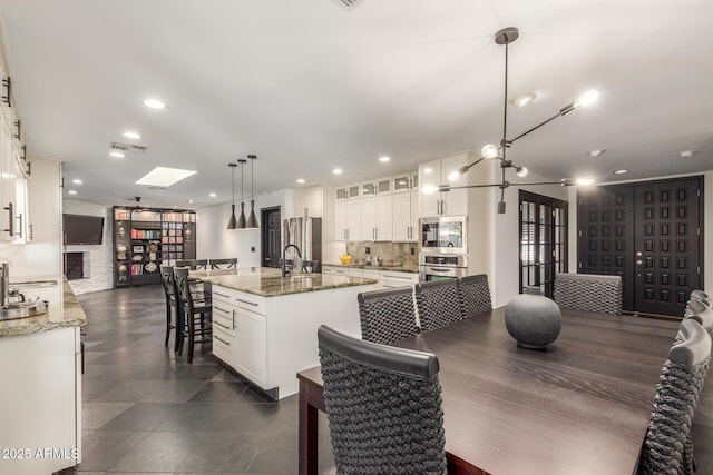 kitchen with visible vents, decorative backsplash, appliances with stainless steel finishes, a kitchen island with sink, and white cabinetry