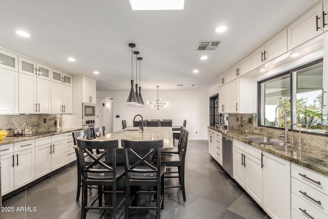 kitchen featuring visible vents, appliances with stainless steel finishes, a kitchen bar, white cabinetry, and a sink