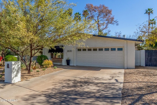 view of front of property featuring concrete driveway, an attached garage, fence, and stucco siding