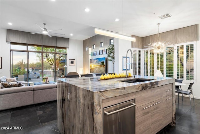 kitchen with pendant lighting, a kitchen island with sink, ceiling fan with notable chandelier, sink, and light stone counters