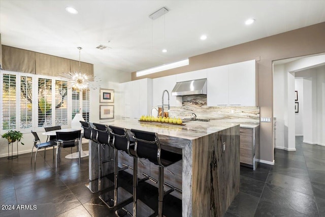 kitchen featuring backsplash, ventilation hood, light stone countertops, decorative light fixtures, and white cabinetry