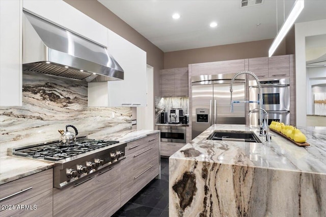 kitchen with light stone countertops, appliances with stainless steel finishes, backsplash, wall chimney exhaust hood, and sink