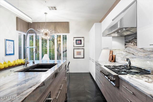 kitchen featuring sink, wall chimney range hood, stainless steel gas cooktop, a notable chandelier, and decorative light fixtures