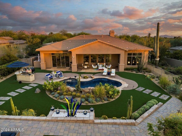 pool at dusk with outdoor lounge area, a yard, and a patio