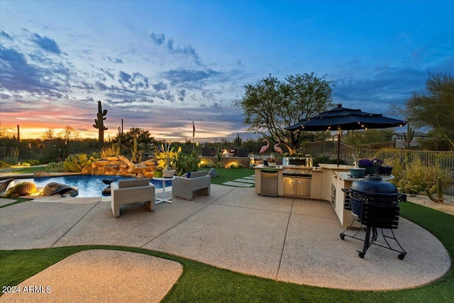 patio terrace at dusk with an outdoor kitchen and a fenced in pool