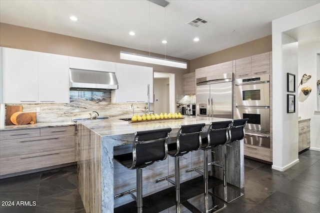 kitchen with tasteful backsplash, a kitchen bar, a kitchen island, exhaust hood, and appliances with stainless steel finishes