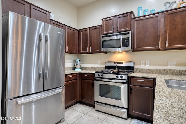 kitchen with appliances with stainless steel finishes, light stone counters, dark brown cabinetry, sink, and light tile patterned floors