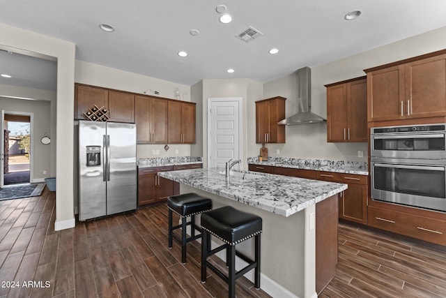 4240 Blacksmith Way, Wickenburg, AZ 85390 - kitchen featuring appliances with stainless steel finishes, wall chimney range hood, a sink, wood tiled floors, and an island with sink