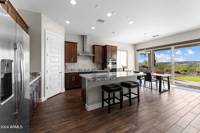 kitchen with wall chimney exhaust hood, dark hardwood / wood-style flooring, a kitchen island with sink, and appliances with stainless steel finishes