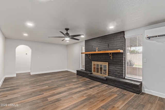 unfurnished living room featuring a wall mounted air conditioner, dark hardwood / wood-style floors, a brick fireplace, and ceiling fan