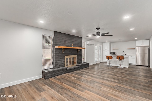 unfurnished living room featuring ceiling fan, plenty of natural light, a brick fireplace, brick wall, and dark hardwood / wood-style floors