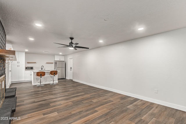 unfurnished living room with ceiling fan, sink, dark wood-type flooring, and a textured ceiling