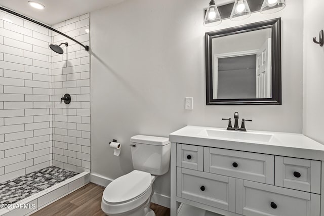 bathroom with toilet, a tile shower, vanity, and wood-type flooring