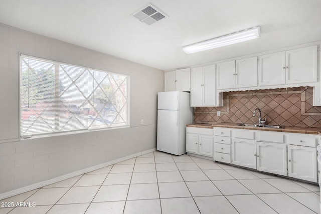 kitchen with white fridge, white cabinetry, tasteful backsplash, light tile patterned flooring, and sink