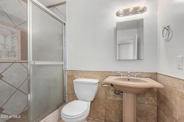 bathroom with sink, tile walls, toilet, and a shower with door