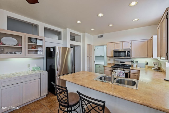 kitchen with kitchen peninsula, sink, light tile patterned flooring, a kitchen bar, and appliances with stainless steel finishes