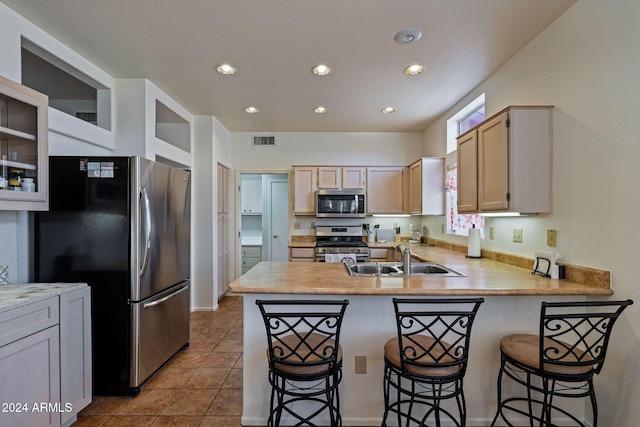 kitchen featuring kitchen peninsula, a breakfast bar, light brown cabinetry, sink, and stainless steel appliances