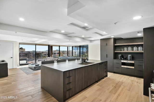 kitchen with light wood finished floors, modern cabinets, an island with sink, and a sink