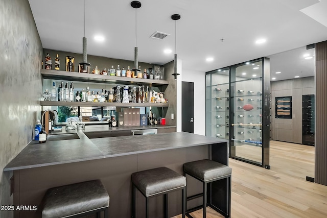 bar featuring visible vents, wet bar, light wood-style floors, hanging light fixtures, and a sink