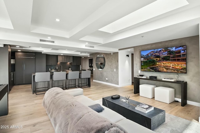 living room with light wood finished floors, visible vents, baseboards, recessed lighting, and a raised ceiling