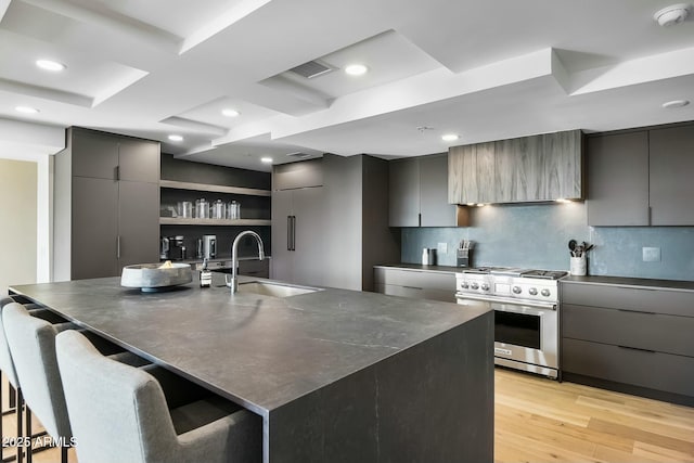 kitchen with dark countertops, light wood-style floors, high end stainless steel range oven, modern cabinets, and a sink