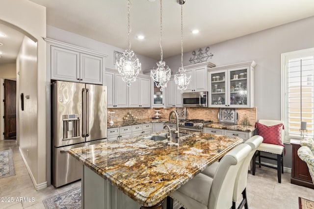 kitchen featuring an island with sink, premium appliances, backsplash, arched walkways, and glass insert cabinets