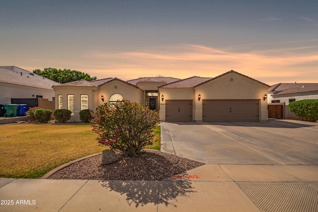 mediterranean / spanish-style home featuring stucco siding, a tile roof, a lawn, and a garage