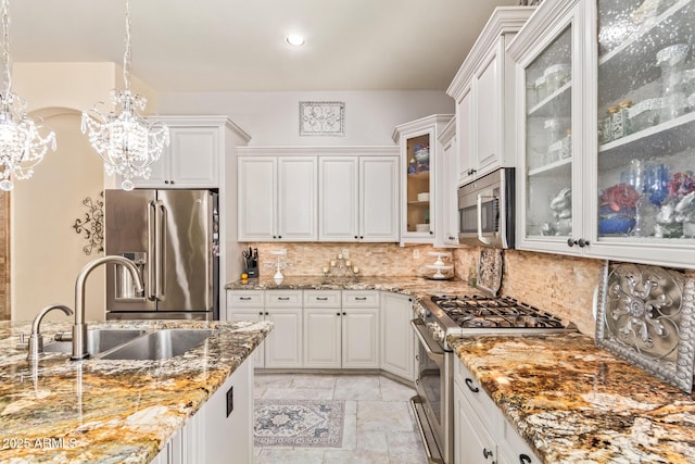kitchen with a notable chandelier, a sink, tasteful backsplash, appliances with stainless steel finishes, and light stone countertops
